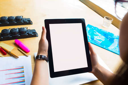 Female successful financier using digital gadget computer with empty mockup copy space screen background for advertising text message, sitting at desktop with paper documents and working toolsの写真素材