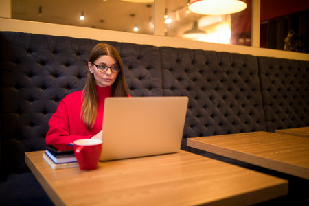 Serious woman successful blog editor having online work on notebook gadget while sitting in coffee shop interior near copy space for advertisingの写真素材
