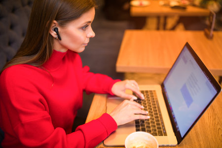 Female smart commercial real estate analyst checking e-mail on laptop computer while sitting in coffee shop during work break.の写真素材