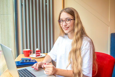 Young female in glasses experienced business plan writer looking in camera while sitting with portable laptop computer in restaurant interiorの写真素材