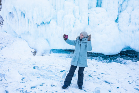 Happy smiling female wonderer talking via mobile phone call while standing against big ice on the big rocksの写真素材