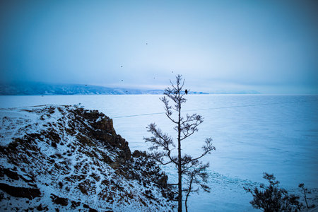 Rock montain on the shore of the frozen winter lake Baikal in cloudy foggy winter day. Winter Siberian landscape. Ogoy Island on Lake Baikal.の写真素材