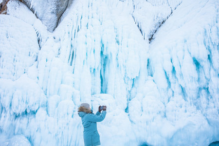 Female wonderer shooting video on smartphone of a big ice rock during winter adventure on Baikal lakeの写真素材