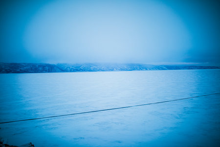 View of snowy mountains and frozen Lake Baikal in a gloomy winter dayの写真素材