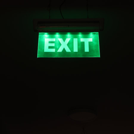 Green exit sign letters symbol glowing in the dark emergency escape way. Escape from darkness in the light concept ideaの写真素材