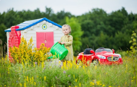 little girl watering flowers in front of his houseの写真素材