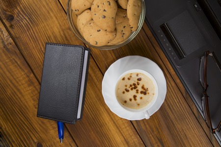 computer, a cup of coffee and cookies on wooden tableの写真素材