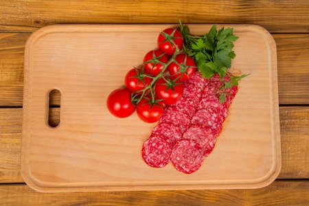 tomatoes with sliced sausage on a wooden trayの写真素材