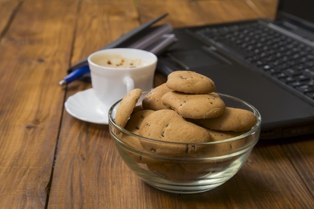 computer a cup of coffee and cookies on wooden tableの写真素材