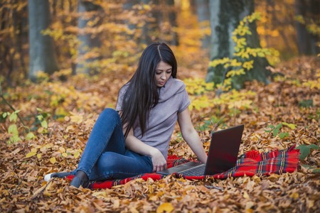 beautiful girl with a laptop in the autumn forestの写真素材