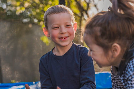 A boy and a girl happily sitting on a trampoline together outdoorsの写真素材