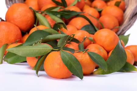 Ripe tangerines with leaves in a basket on a white backgroundの写真素材