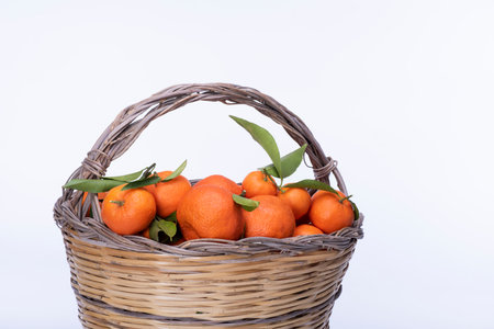 Ripe tangerines with leaves in a basket on a white backgroundの写真素材