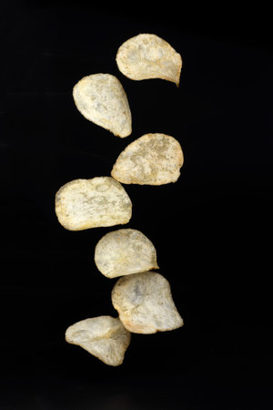 Stack of tasty potato chips falling on black backgroundの写真素材