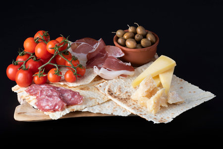 Italian antipasti on a wooden board on a black backgroundの写真素材