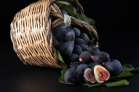Fresh ripe figs in a basket on a black background with leavesの写真素材