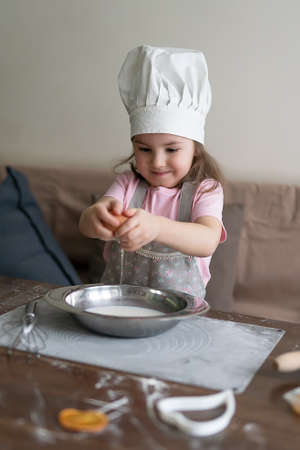 A cute little girl in a chef's hat is cooking a cake at the kitchenの写真素材