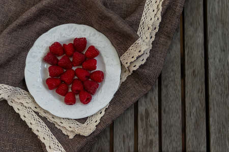 Fresh raspberry in the white plate settled on wooden table with tablecloth