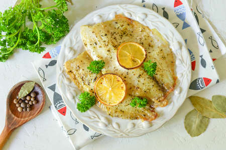 Fried fish fillet with lemon and parsley on a white plateの写真素材
