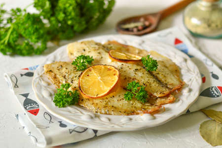 Baked fish with lemon and parsley on a white plate.の写真素材