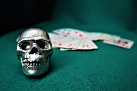 Small decorative silver human skull with playing cards on a green tableの写真素材