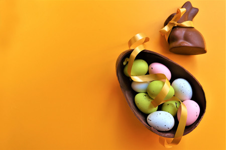 Colored chocolate Easter eggs and chocolate bunny with copy space on a yellow backgroundの写真素材