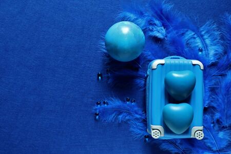 two blue hearts and suitcase on blue bird feathers in trendy color of year 2020 on classic blue background. Copy space.の写真素材