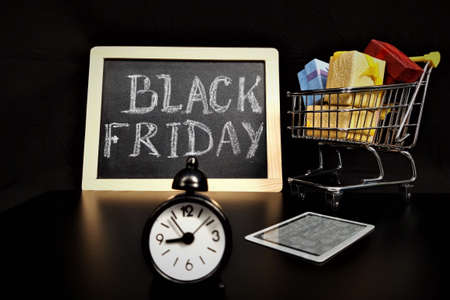 Black friday concept on black background. Multi-colored gift bags, shopping cart, credit card,...