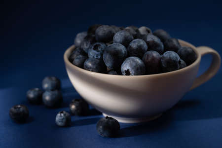 Cup of fresh blueberry fruit in dark and moody lighting. Dark blue backgroundの写真素材