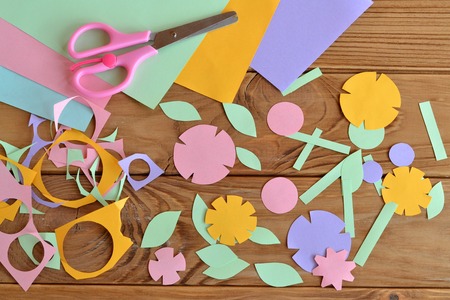 Paper flowers, paper sheets, scissors, paper scrap on a wooden table. Paper flower craft for kids....