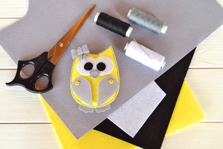 Felt owl toy. Children's crafts idea project. Felt sheets, scissors, thread, needle, pins - a set for needlework. Wooden backgroundの写真素材