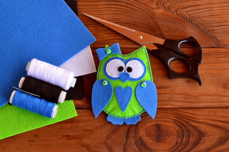 Felt owl pattern, bird toy play, owl ornaments, sewing plush toy. Hand fabric diy. Felt animal gift. Scissors, thread, needle, colorful sheets of felt on a wooden tableの写真素材