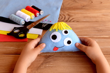 Child holds a felt monster in his hands. Funny soft toy for kids. Sewing craft supplies and tools on...