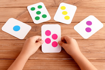 Little girl holds a flash card in his hands and learns the color, shape, quantity. Colorful flash cards for fun teaching children. Early childhood development concept. Wooden backgroundの写真素材