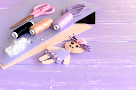 Creative art and craft idea for children. Felt doll, scissors, thread, needles, pins, suede cord, felt sheets on wooden background with empty place for text. Set to create children toyの写真素材