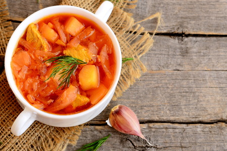 Homemade cabbage soup with meat and vegetables in a bowl, garlic on old wooden background. Dinner or lunch menu recipe. Closeup. Top view