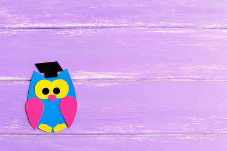 Colored cardboard owl isolated on a lilac wooden background with empty place for text. Bright owl made of colored cardboard. School backgroundの写真素材