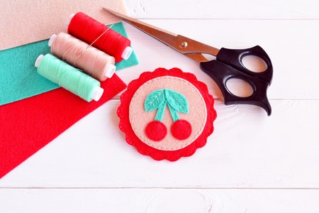 Colorful felt brooch. Brooch felt embroidery. Brooch with cherries. Summer kids crafts. Beautiful handicraft. Sheets of felt, scissors, thread, needle - sewing kitの写真素材