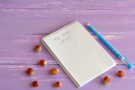 Paper notebook, pen, nuts on lilac wooden background. My diet plan. Slimming concept. Lifestyle. A notepad diet menu. Copybook for diets programsの写真素材
