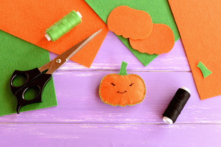Easy sew stuffed fabric pumpkin decoration, threads, scissors, needle, felt sheets and patterns on lilac wooden table. Halloween pumpkin idea made with felt. Kids Halloween backgroundの写真素材