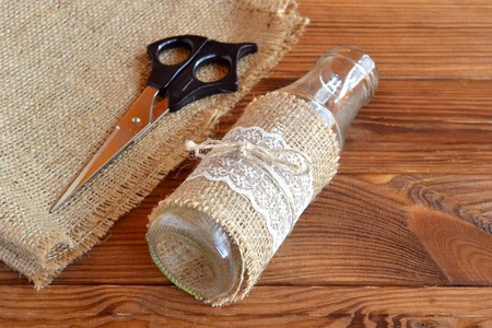 Handmade vase. Easy crafts. Rustic style. Glass bottle, scissors, burlap. Brown wooden backgroundの写真素材