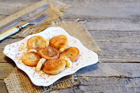 Fried bananas in batter on a plate, fork, knife, burlap on wooden background with copy space for text. Vegetarian banana fritters recipe. Vintage style. Closeupの写真素材