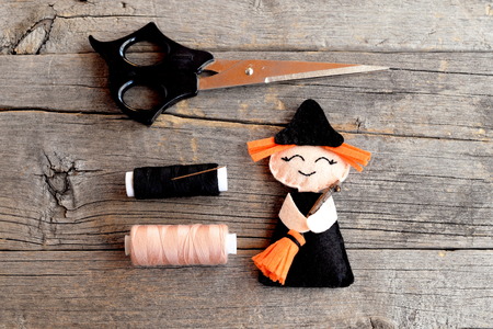 Halloween felt witch with broom, beige and black thread, needle, scissors on old wooden background....