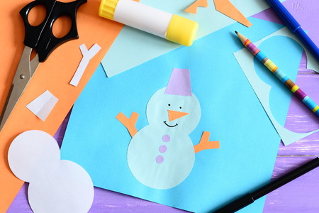 Paper card with snowman applique and text I love winter. Scissors, glue stick, pencil, markers, paper sheets and scraps on wooden background. Simple and fun kids winter crafts. Top viewの写真素材