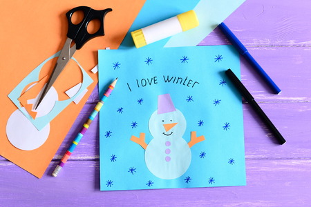 Making a children winter paper cards. Step. Paper card with snowman collage and text I love winter. Stationery and materials on wooden background. Kids winter crafts concept. Closeup. Top viewの写真素材