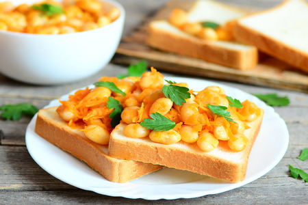 Baked white beans on toast. Beans baked with carrots, garlic and tomato sauce and garnished with fresh parsley. Homemade vegetarian white beans recipe. Closeupの写真素材
