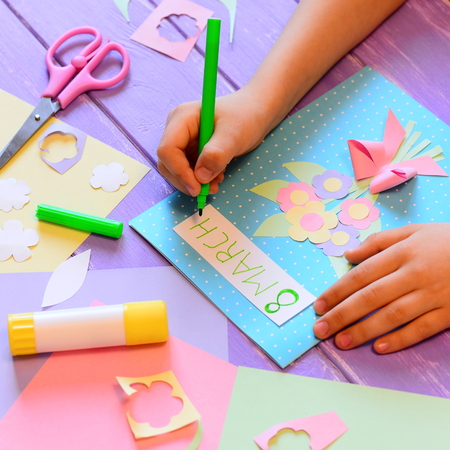 Creating a greeting card with flowers for mom. Child holds a pen in hand and writes March 8. Tools and materials for children's art activity. March 8 greeting card crafts conceptの写真素材