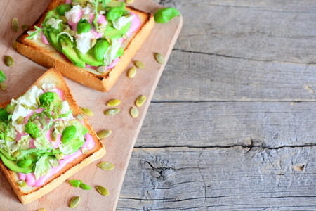 Avocado sandwiches on a wooden board and on a vintage background with copy space for text. Homemade open sandwiches with avocado, pumpkin seeds, lettuce, basil and cream. Healthy foodの写真素材