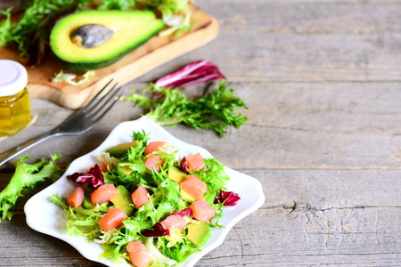 Smoked salmon, lettuce, avocado salad with lemon and olive oil dressing on a plate. Quick and delicious salmon salad recipe. Wooden background with copy space for textの写真素材
