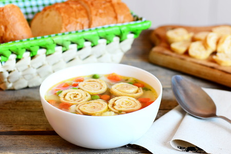 Delicious soup with vegetable mix and fried omelette in a bowl. Bread slices, spoon on a rustic wooden background. Healthy soup with omelette, carrot, peas, leek, cauliflower and potatoesの写真素材